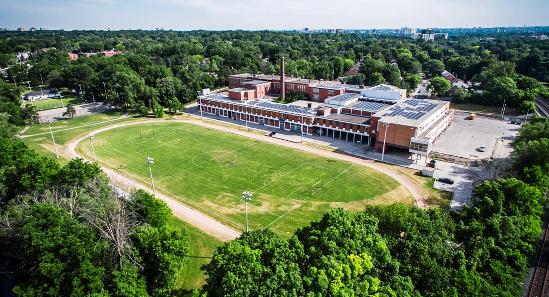 L'imponente edificio in mattoni dell'Etobicoke Collegiate Institute si trova davanti a un prato verde con un bosco sullo sfondo.