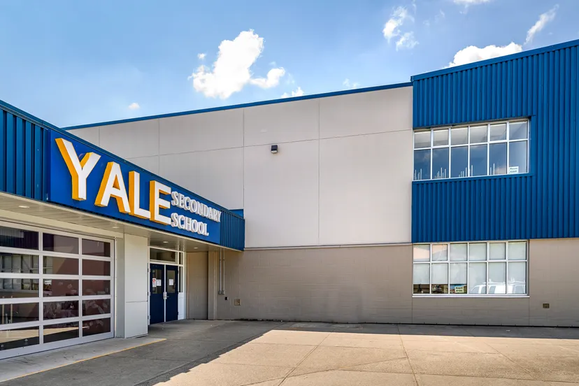 Il grande complesso industriale bianco e blu della Yale Secondary School sotto un cielo nuvoloso.