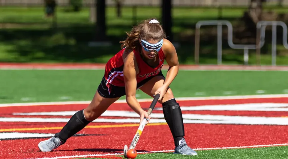 Una studentessa della Kingswood Oxford in abbigliamento sportivo è pronta sulla pista d'atletica con una mazza da hockey.