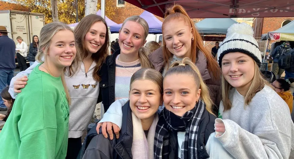 Un gruppo di giovani studentesse si trova nel campus del Launceston College davanti a foglie autunnali colorate.