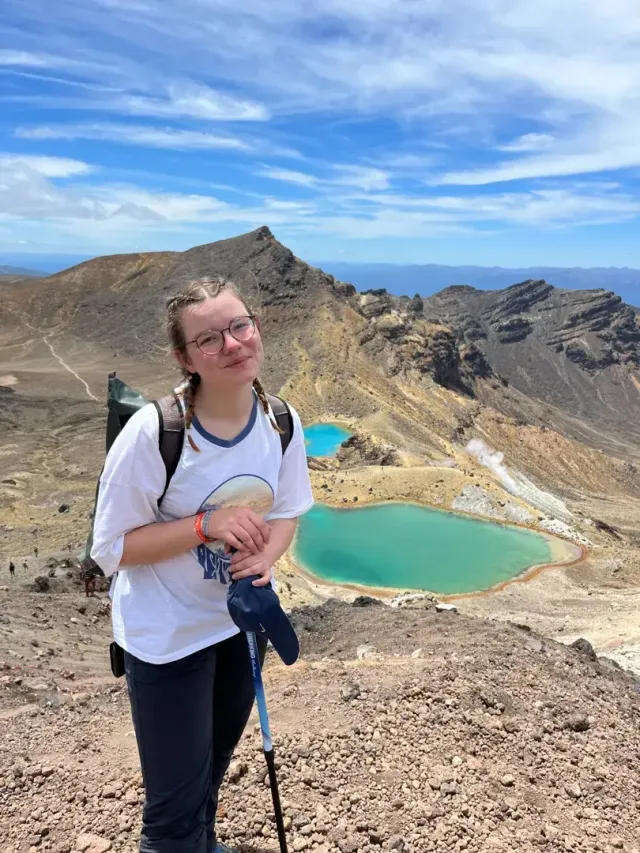 Studentessa in escursione con zaino e bastoncini davanti a laghi vulcanici colorati in Nuova Zelanda