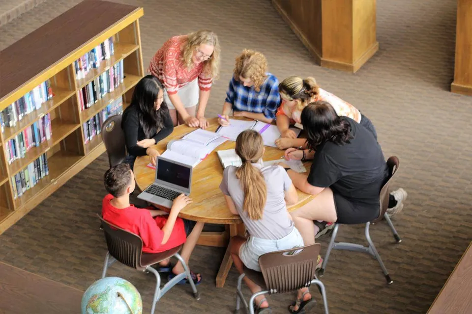 Studenti della The Orme School siedono a un tavolo in biblioteca e lavorano insieme a un compito.