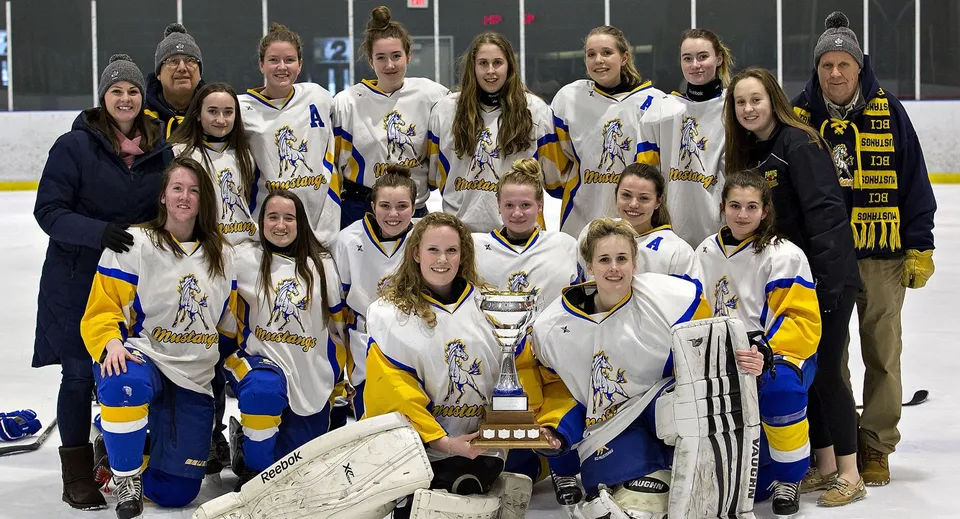 Un gruppo di giovani giocatrici di hockey del Rosseau Lake College posa insieme a una coppa in una pista di ghiaccio.
