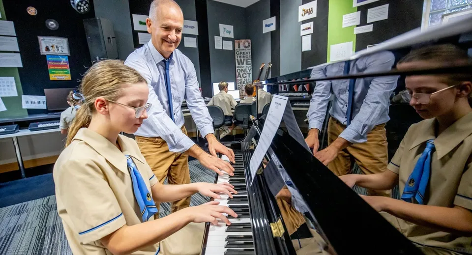 Una giovane donna suona il pianoforte mentre studenti e insegnanti della All Saints Anglican School ascoltano.
