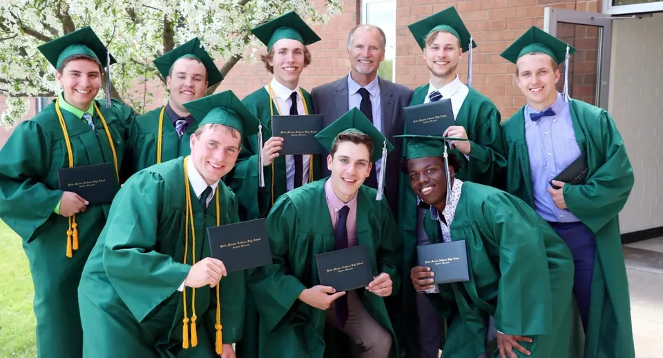Diplomati e diplomate della Kettle Moraine High School indossano toghe verdi davanti a un edificio in mattoni, tenendo in mano i loro diplomi.