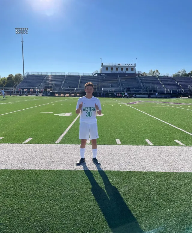 Estudiante con equipación de fútbol americano levanta los pulgares ante las gradas de un estadio