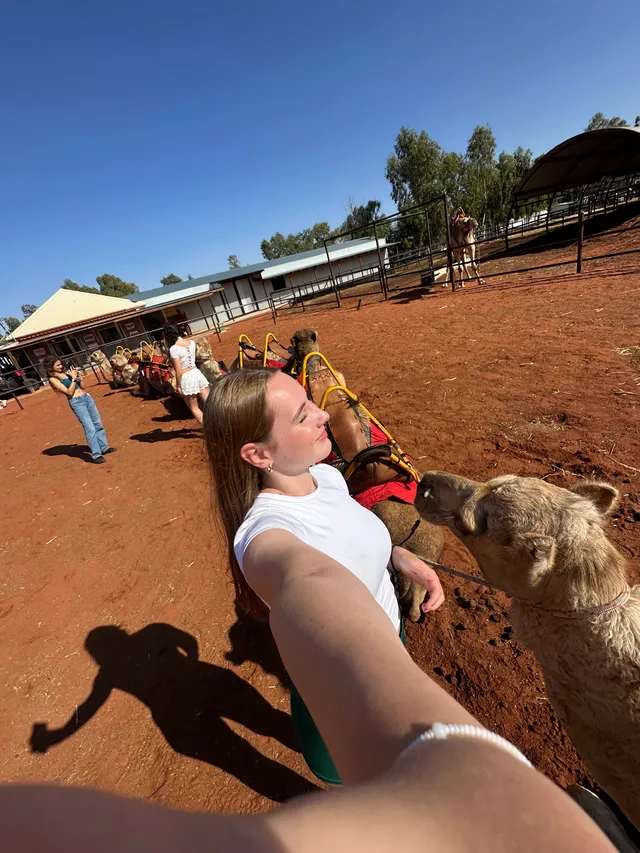 Selfie de una chica junto a un camello en un recinto de tierra roja del interior de Australia