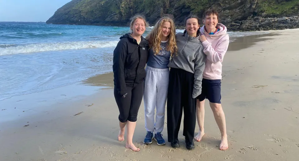 Quattro studentesse del St. Columba's College si trovano insieme sulla spiaggia con vista sul mare e su scogliere rocciose.