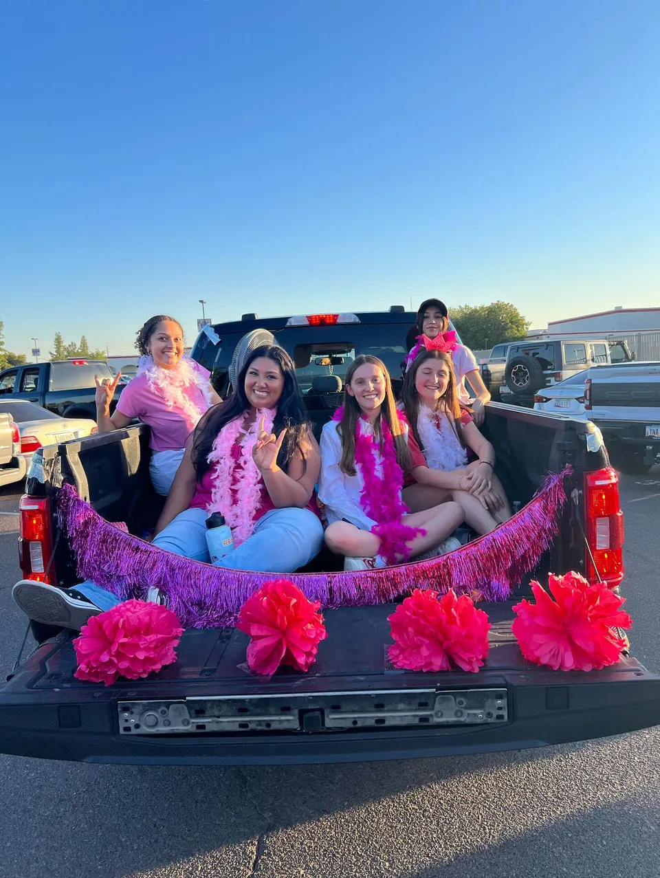 Cinque studentesse della Mountain View High School siedono con boa rosa sul cassone di un pickup decorato.