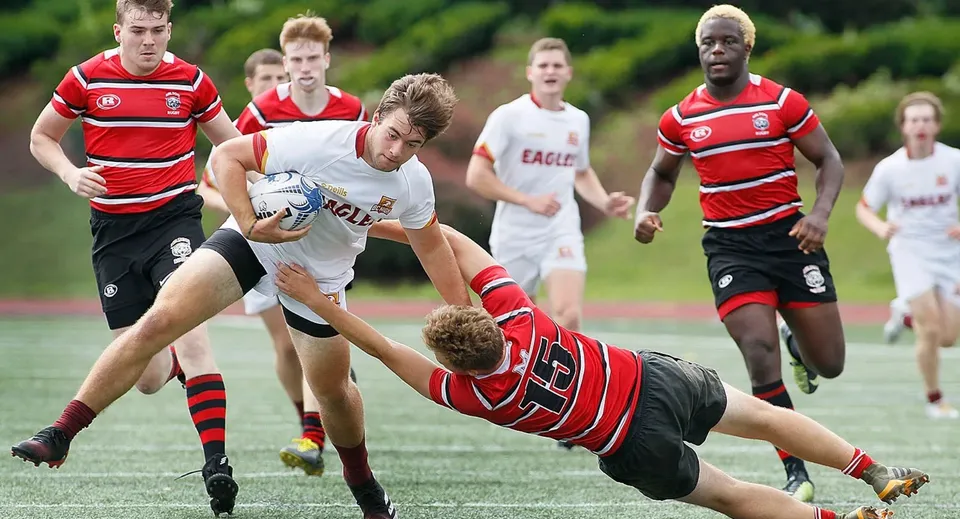 Studenti della Burnie High School giocano una partita di rugby sul campo sportivo con giocatori in maglia rossa e bianca.