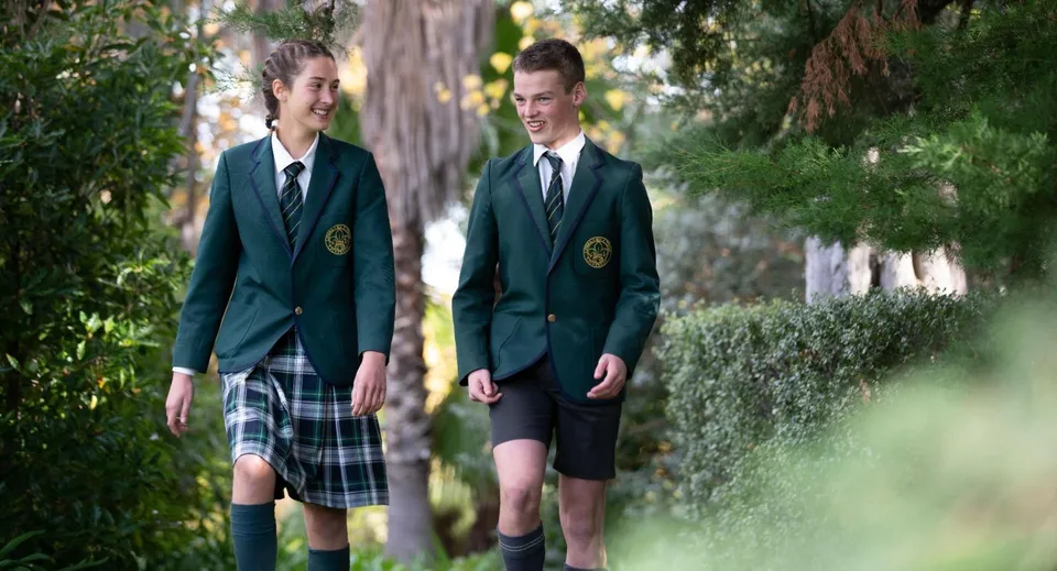 Due studenti in uniforme scolastica camminano insieme su un viale circondato da una lussureggiante vegetazione nel campus del Mercedes College.