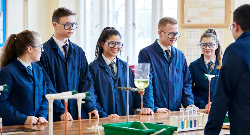 Studenti in toghe accademiche intorno a un tavolo con attrezzature scientifiche nel laboratorio del Clifton College.