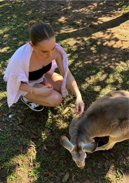 Alicia hockt sich hin und streichelt ein grasendes Känguru in Australien