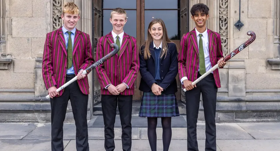 Quattro persone in abito formale sono in piedi davanti a un edificio nel campus del Fettes College.