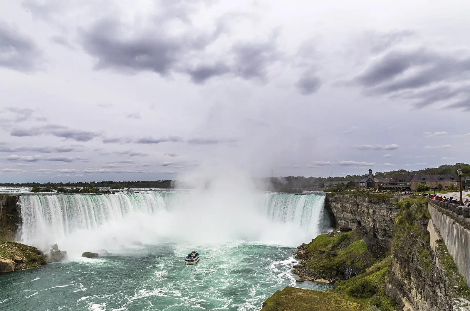 Niagarafälle mit Ausflugsboot in der aufsteigenden Gischt unter bewölktem Himmel