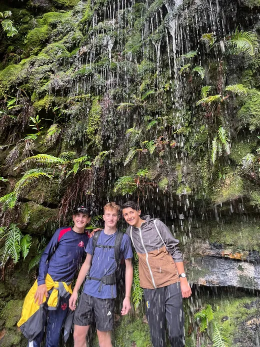 Tre studenti sorridono sotto una cascata tra felci e rocce muschiose in Sudafrica