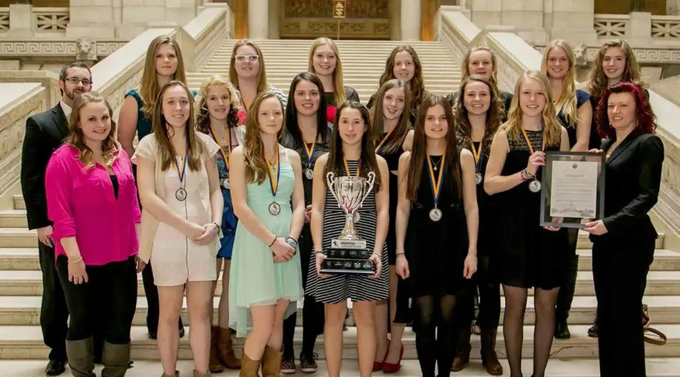 Un gruppo di studentesse della Westwood Collegiate sta insieme a un trofeo davanti a un imponente edificio.