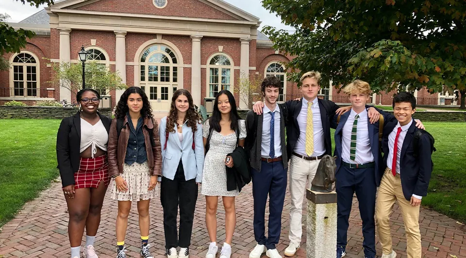 Un gruppo di studenti si trova davanti allo storico edificio della Deerfield Academy circondato da un paesaggio verde.