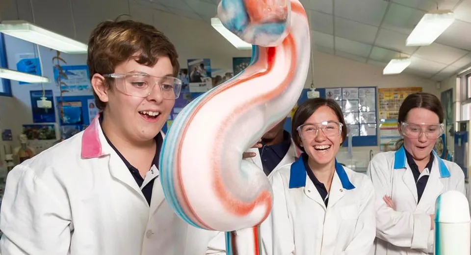 Tre persone in camice bianco da laboratorio con un grande modello di cuore colorato durante la lezione al Hamilton Secondary College.