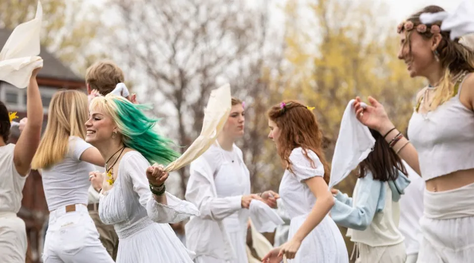 Un gruppo di giovani donne in abito bianco si trova su un campo immerso nella natura all'interno del campus della High Mowing School.