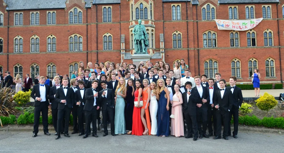 Un grande gruppo di studenti e studentesse in abiti formali si trova davanti a un edificio storico nel campus del Framlingham College.