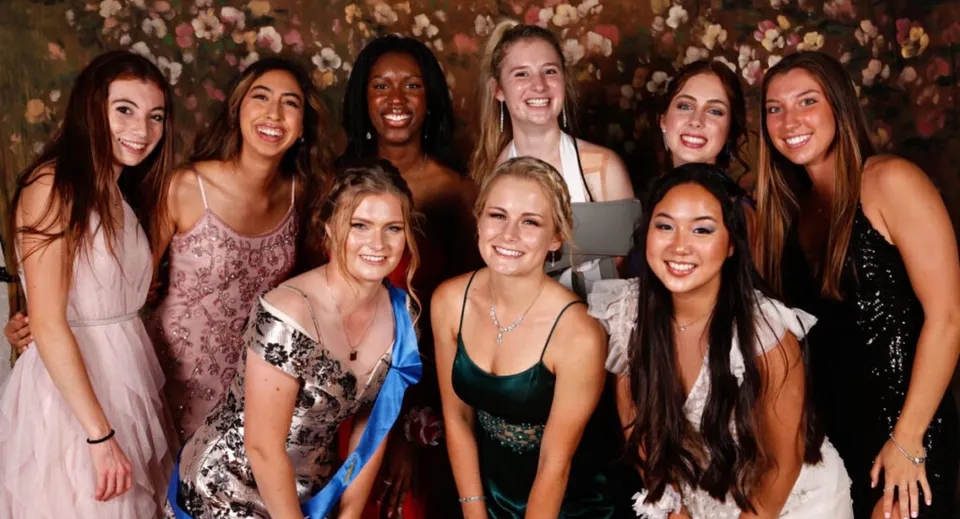 Studentesse della Montverde Academy sorridono in abiti da sera davanti a uno sfondo floreale.