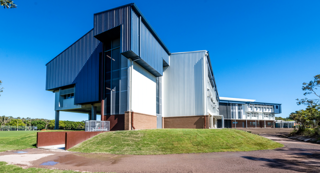 Das moderne Gebäude mit Glas-, Metall- und Backsteinfassade der Mountain Creek State High School steht auf einem grasbewachsenen Hügel.