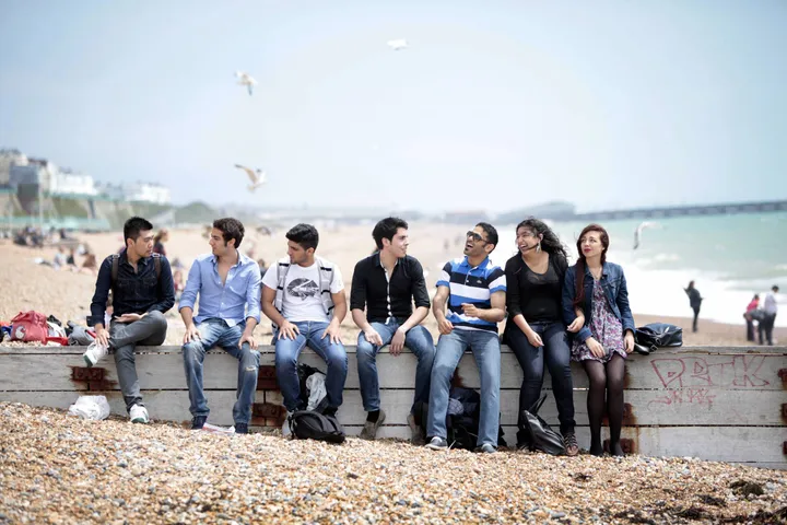 Schüler der Sprachschule sitzen auf der Mauer am Kiesstrand von Brighton
