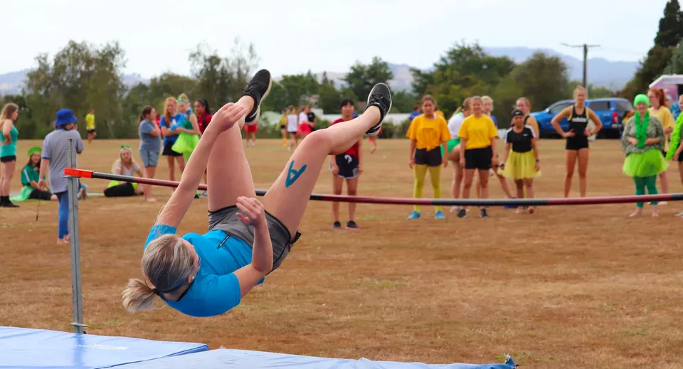 Una studentessa esegue un esercizio di ginnastica su un tappetino nell'area esterna del Waihi College davanti a un gruppo di spettatori.