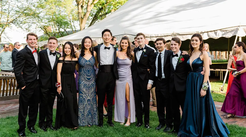 Un gruppo di studenti della Loomis Chaffee School in abbigliamento formale posa all'aperto davanti a una tenda e ad alcuni alberi.