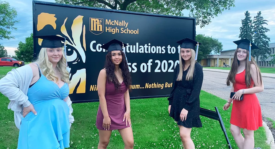 Quattro studentesse posano davanti a un cartello con gli auguri per la classe diplomanda del 2022 della McNally High School.