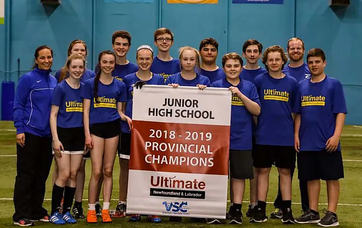 Estudiantes de Mount Pearl Senior High School con pancarta de campeones provinciales 2018-2019 de Ultimate frente a una pared azul.