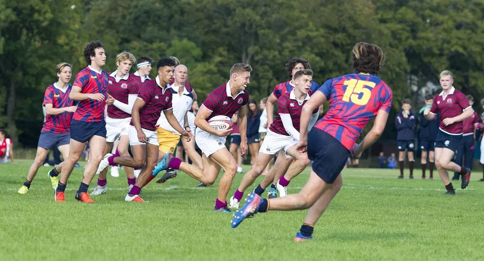 Studenti del Fettes College giocano una partita di rugby su un campo erboso con alberi sullo sfondo.