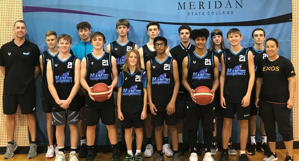 Un gruppo di giovani giocatori e giocatrici di basket posa davanti a uno striscione del Meridan State College.