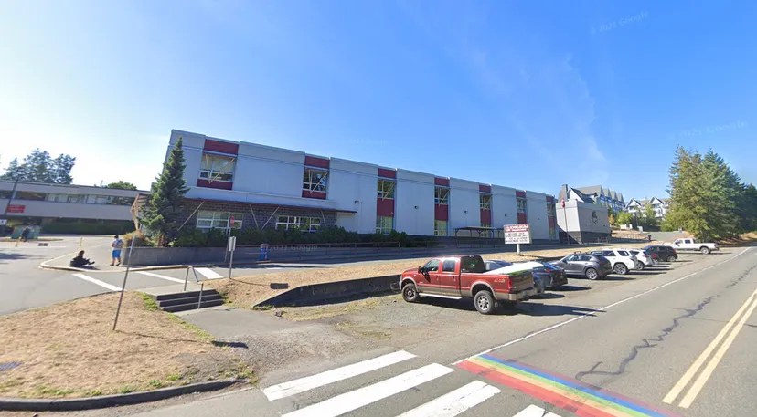 L'edificio a più piani della Kwalikum Secondary School con facciata rossa e bianca è circondato da veicoli parcheggiati.