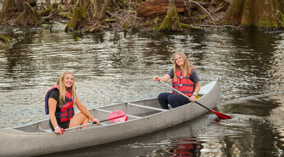 Due studentesse della Trinity Preparatory School pagaiano in canoa su un fiume indossando giubbotti salvagente.