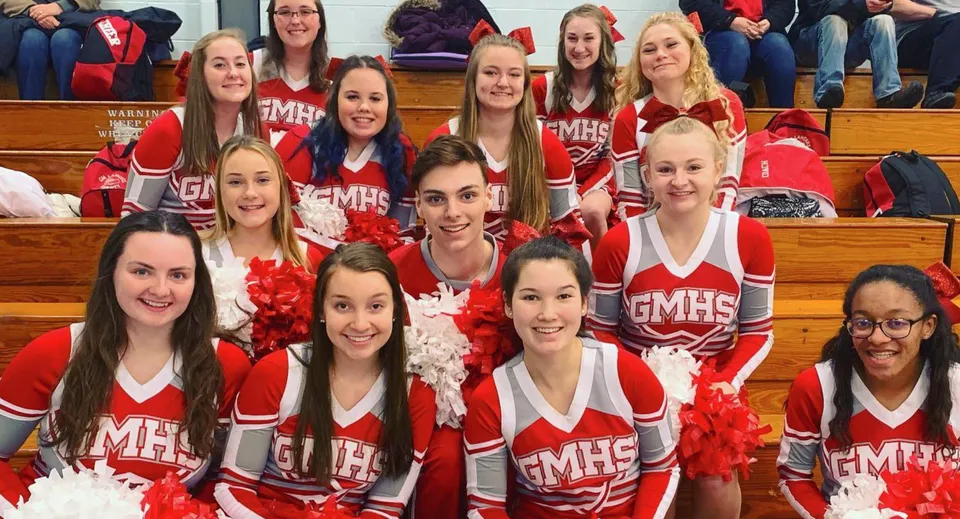 Un gruppo di cheerleader in divisa rossa e bianca posa con i pompon nella palestra della Grand River Academy.