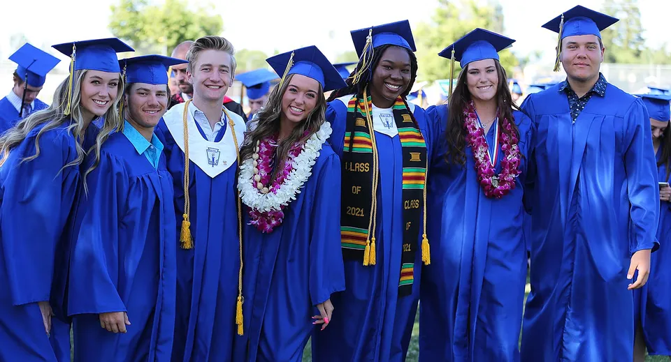 Un gruppo di diplomati con toghe blu si trova all'aperto, nel verde, sul campus della Bakersfield Christian.