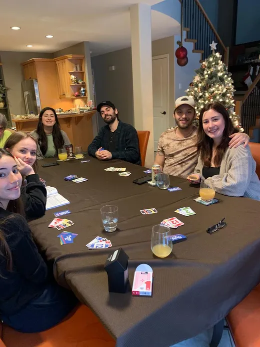Estudiantes y familia anfitriona juegan a las cartas alrededor de una mesa, con un árbol de Navidad al fondo