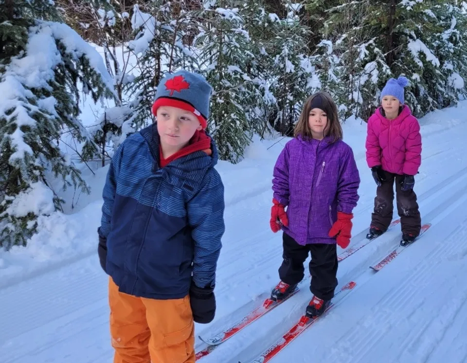 Tre persone in abiti invernali caldi si trovano su un sentiero innevato circondate da pini coperti di neve nel terreno della École Franco-Nord.
