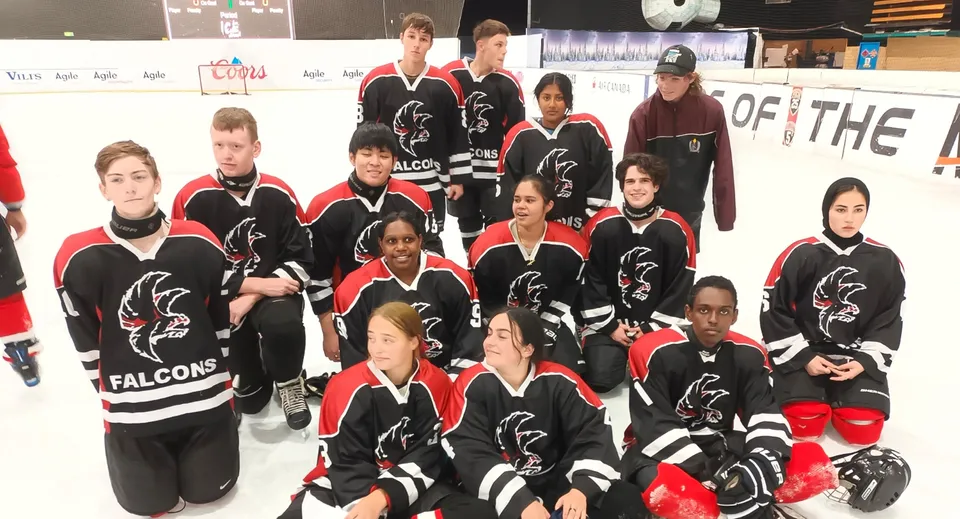 Un gruppo di giovani giocatori di hockey in divisa nera e rossa posa sul ghiaccio della Findon High School.