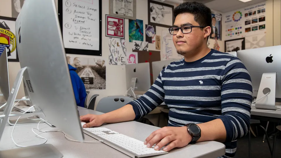 Uno studente del Denver Public School District è seduto concentrato al computer in una stanza con varie opere d'arte.