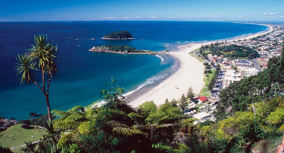 Un paesaggio costiero con una spiaggia a forma di mezzaluna e acque turchesi sullo sfondo di montagne, situato presso l'ACG Tauranga.