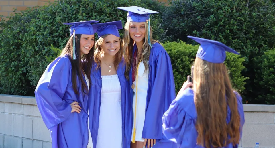 Quattro studentesse della Notre Dame de la Baie Academy in toga da diploma stanno insieme davanti a uno sfondo verde.