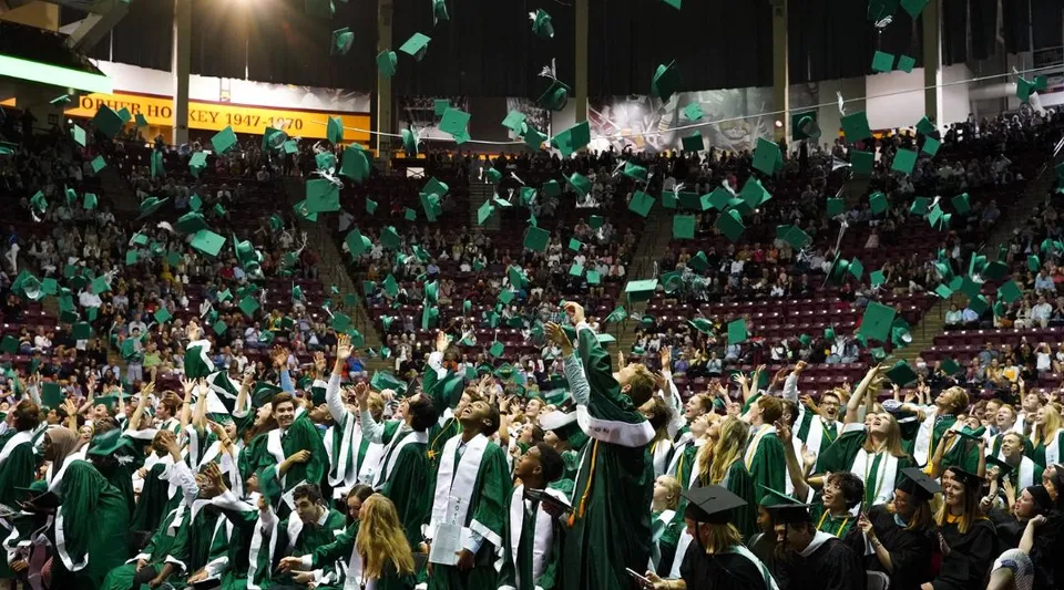 Un grande gruppo di studenti delle Edina Public Schools indossa toghe e tocchi verdi durante una festa nello stadio.