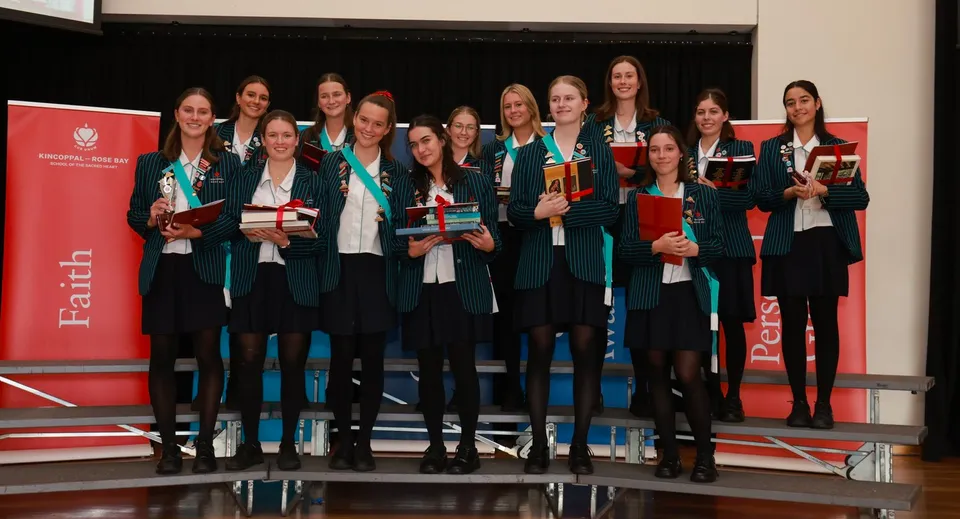 Un gruppo di diplomate della Kincoppal-Rose Bay su uno sfondo rosso con in mano i loro diplomi.