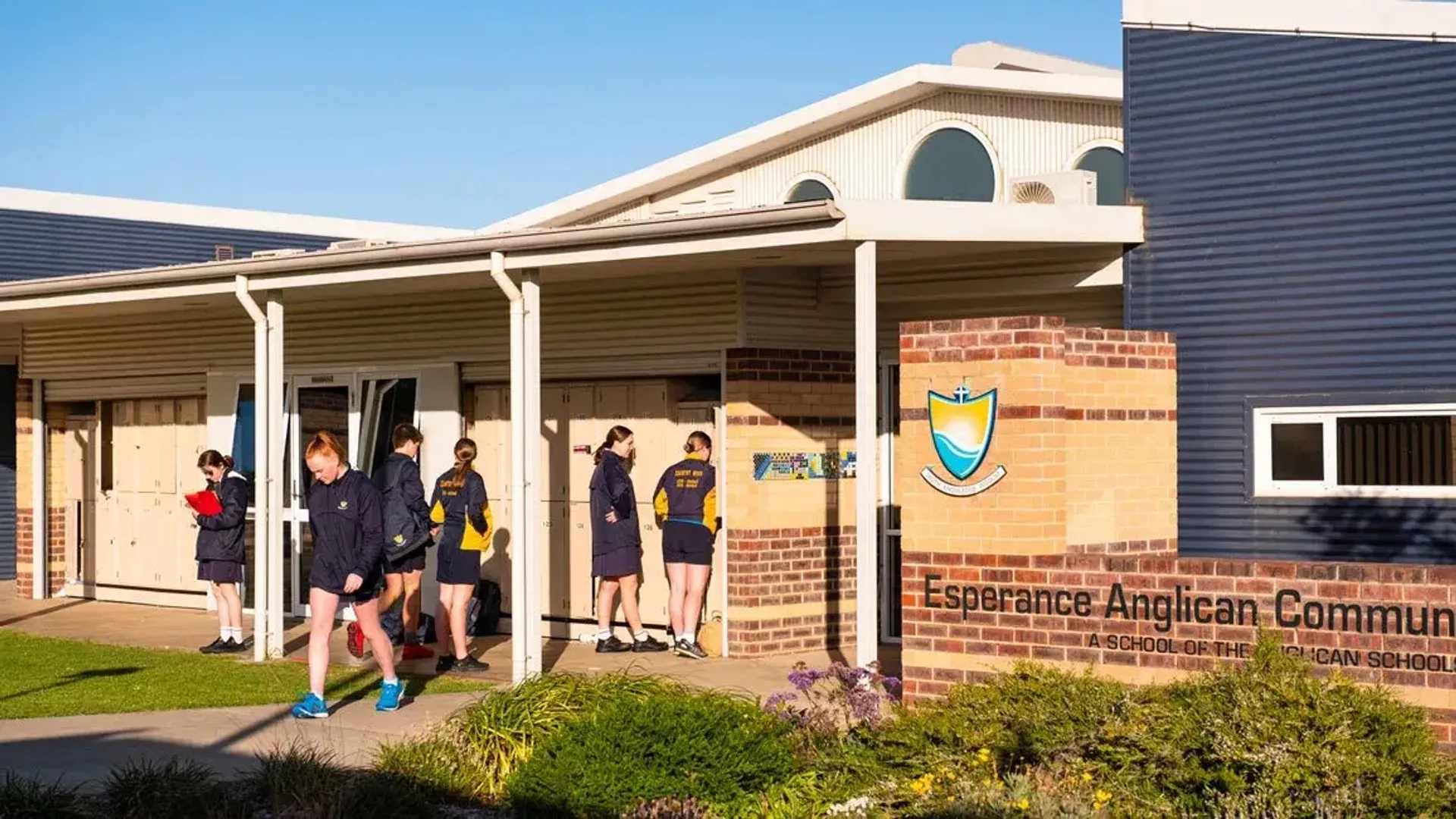 Studenti in divisa scolastica camminano davanti all'ingresso della Esperance Anglican Community School.