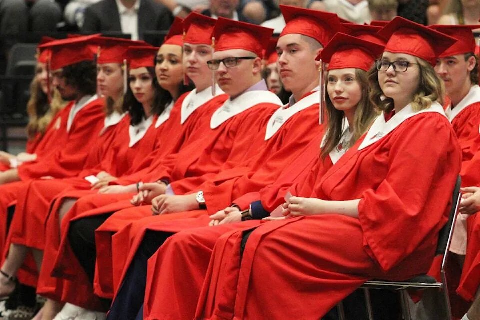 Un gruppo di diplomati e diplomate della Lindsay Thurber Comprehensive High School siede in toga rossa durante la cerimonia di diploma.