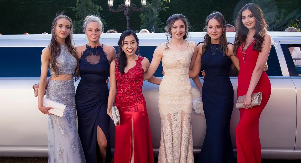 Sei donne vestite in modo elegante del Malvern College posano davanti a una limousine nel verde.