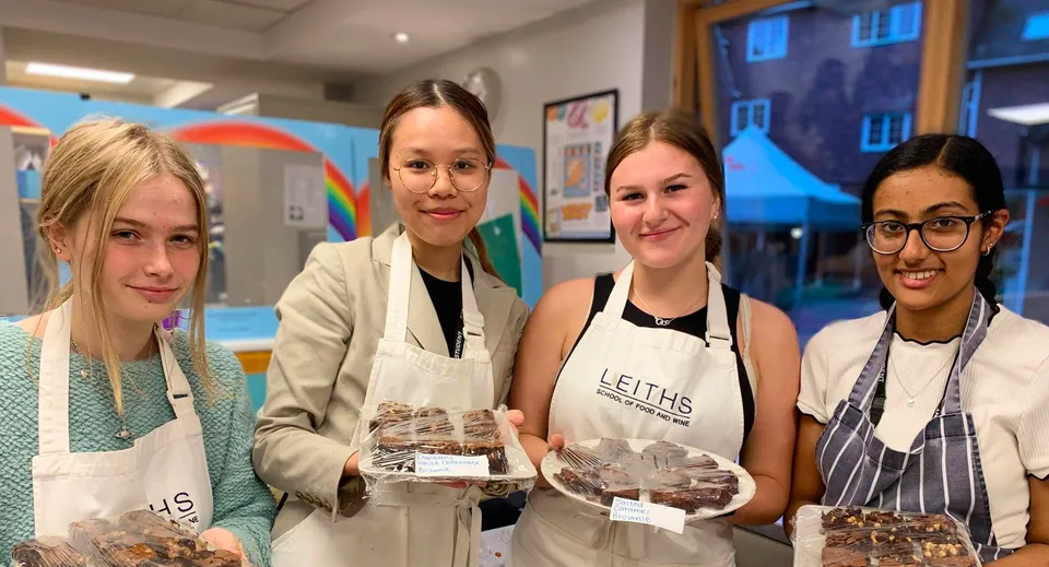 Quattro studentesse della Rye St. Antony School indossano il grembiule e presentano prodotti da forno in una colorata cucina scolastica.